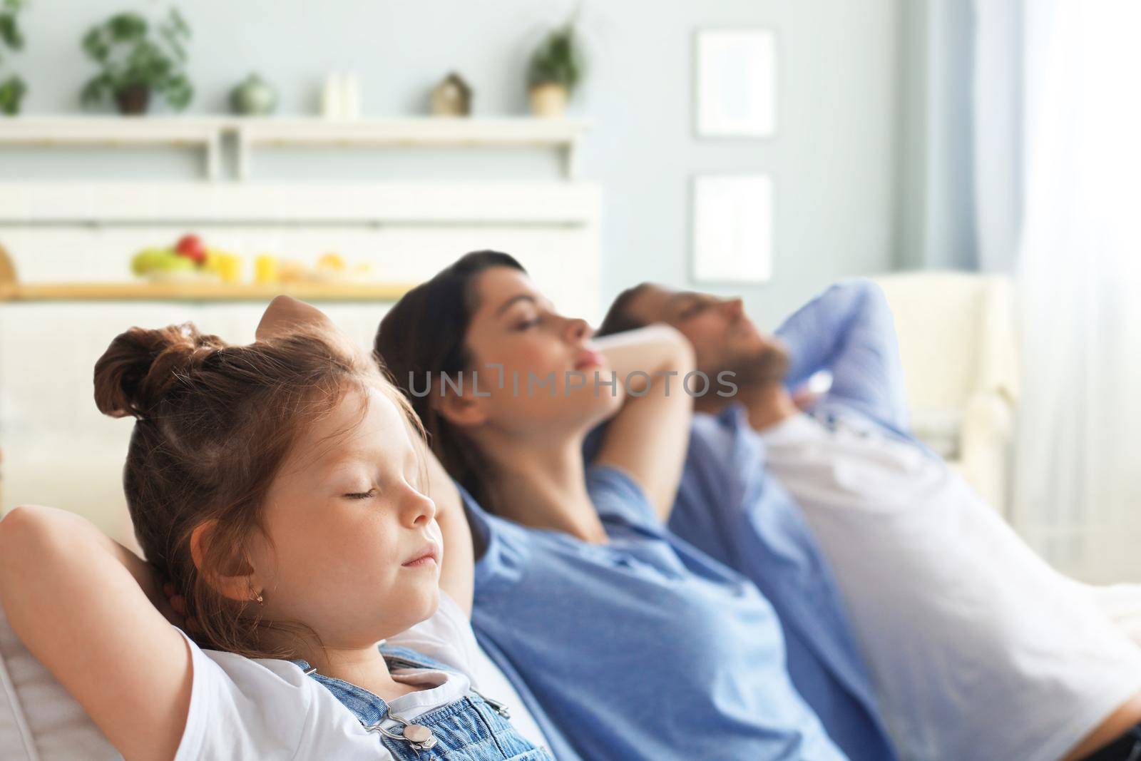 Relaxed young family resting and dreaming about new home on comfortable sofa together at home, happy young parents with little daughter relax enjoying nap relaxing or meditating. by tsyhun