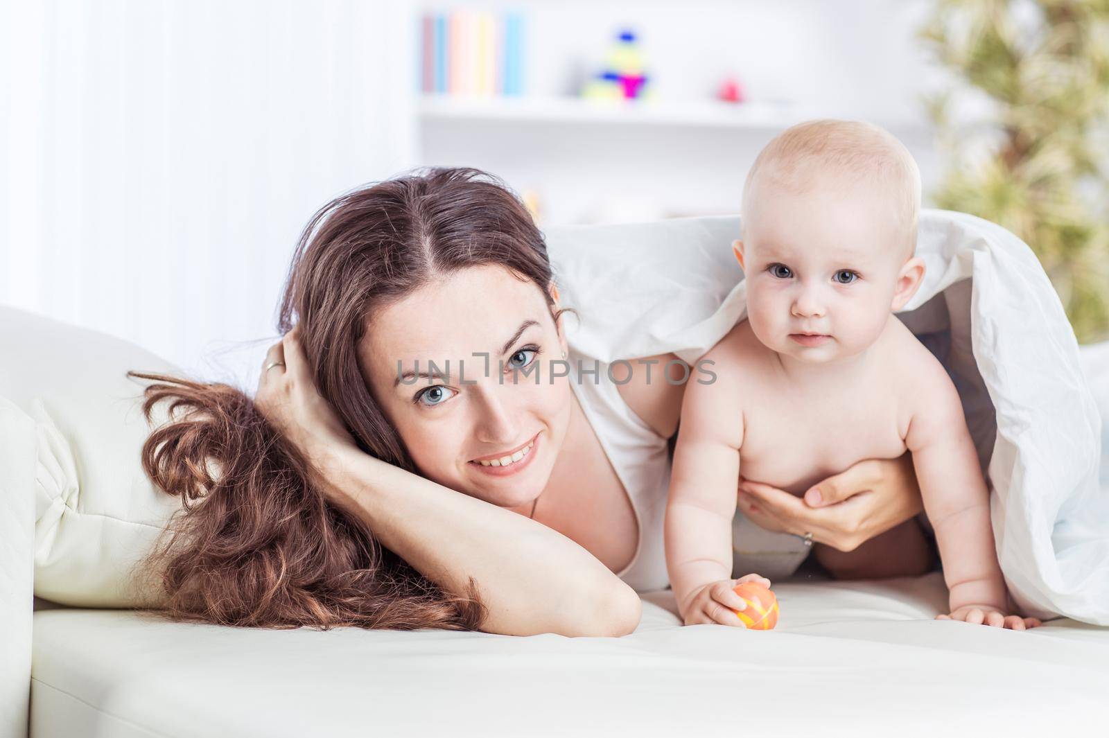 concept of happy mothers: happy mother and her year-old child playing on the sofa in the bedroom by SmartPhotoLab