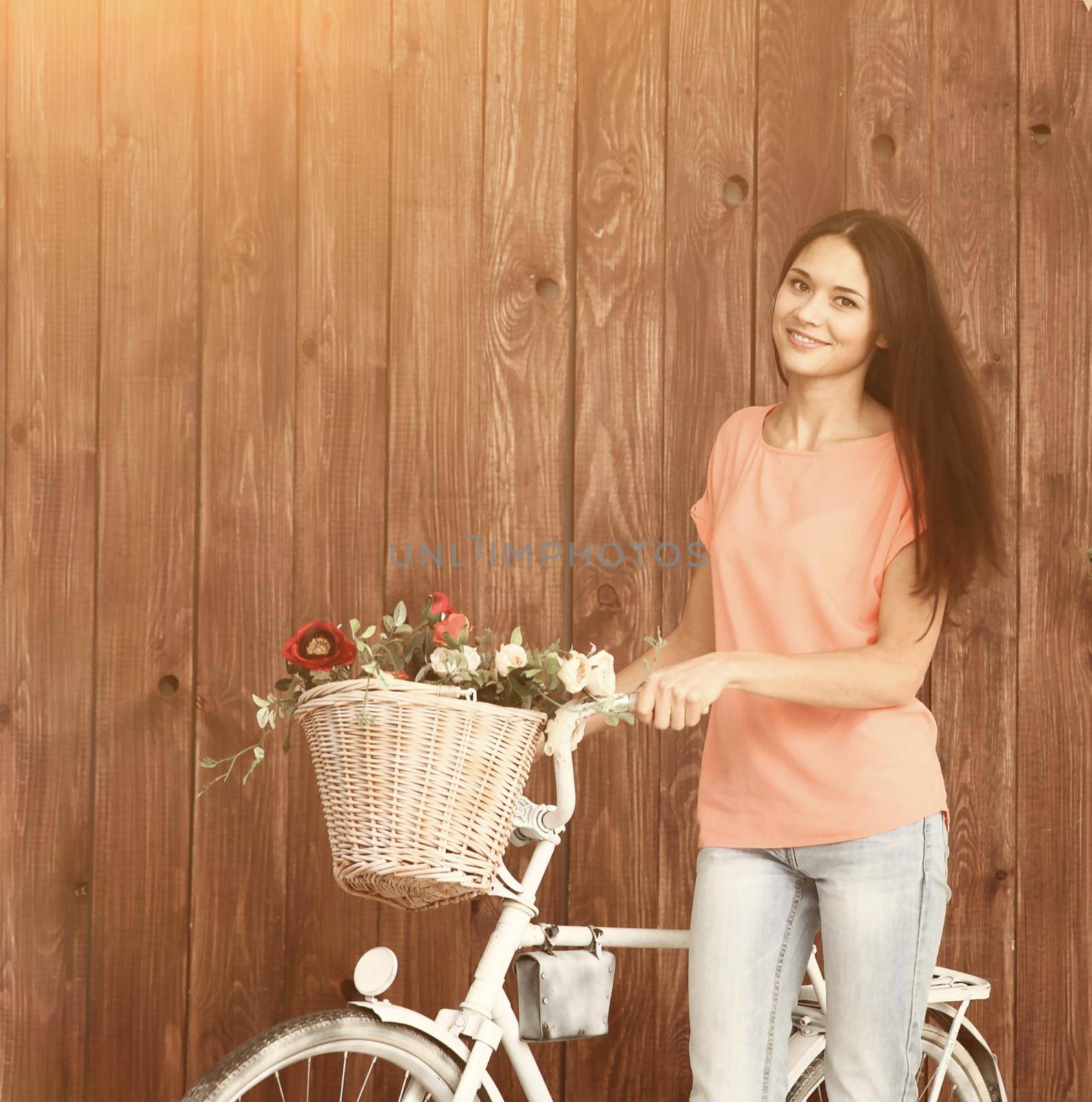 A romantic young woman looking at the camera with her bike and a basket of wildflowers. Summer.
