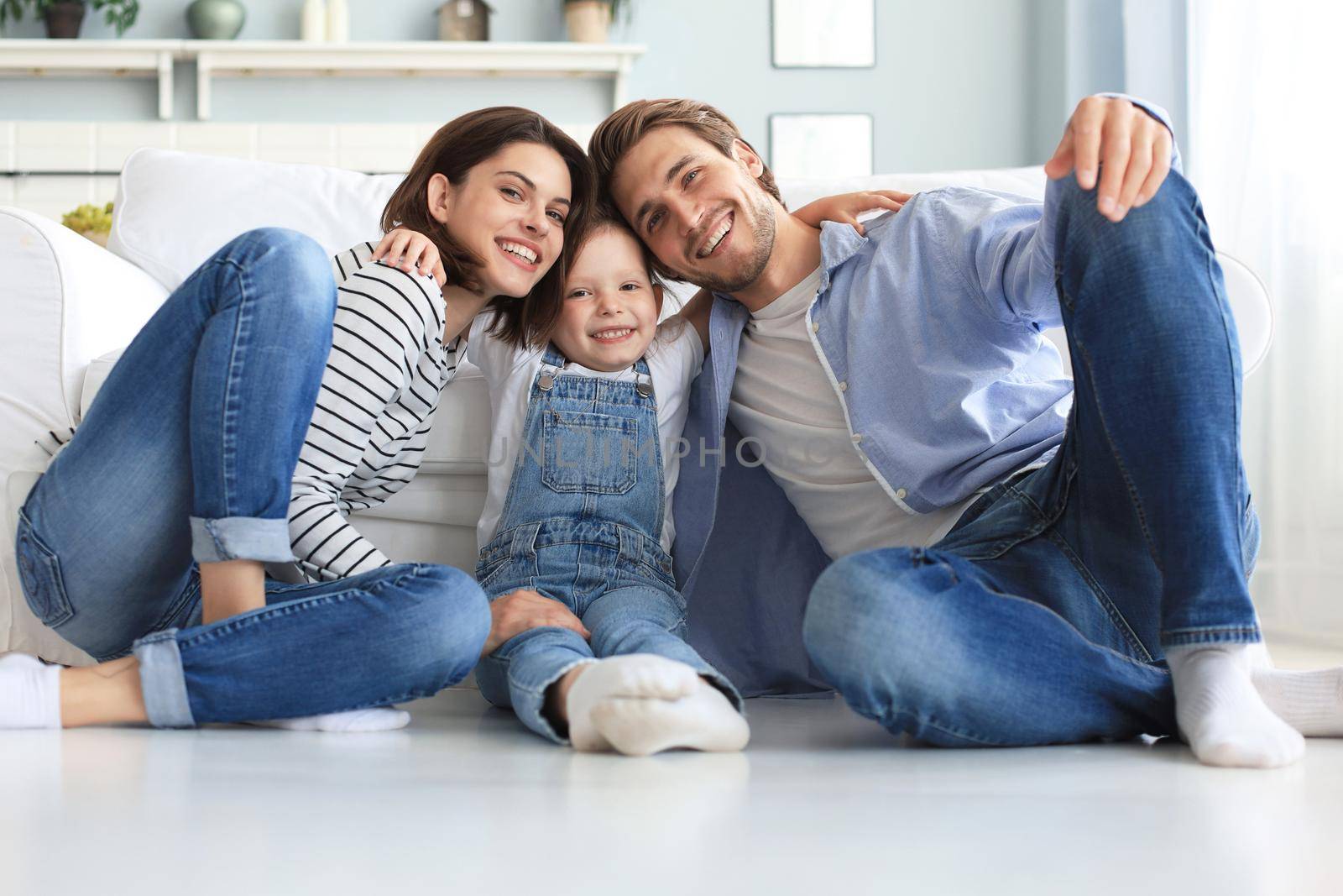 Young Caucasian family with small daughter pose relax on floor in living room, smiling little girl kid hug embrace parents, show love and gratitude, rest at home together