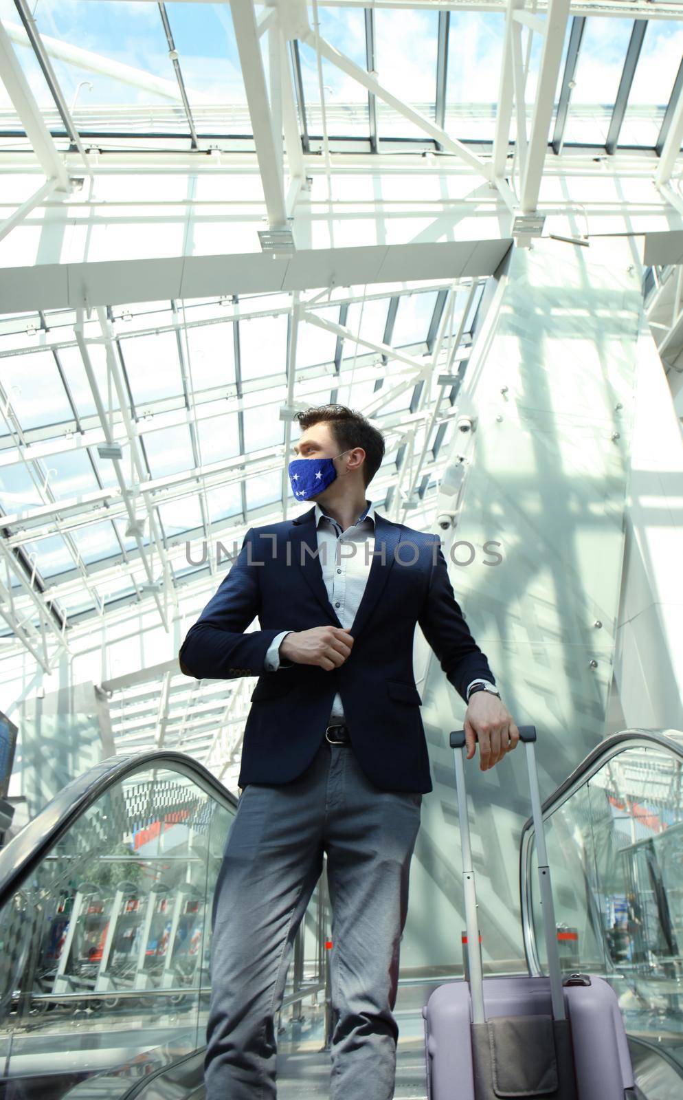 Businessman in protective mask at the airport going down the escalator