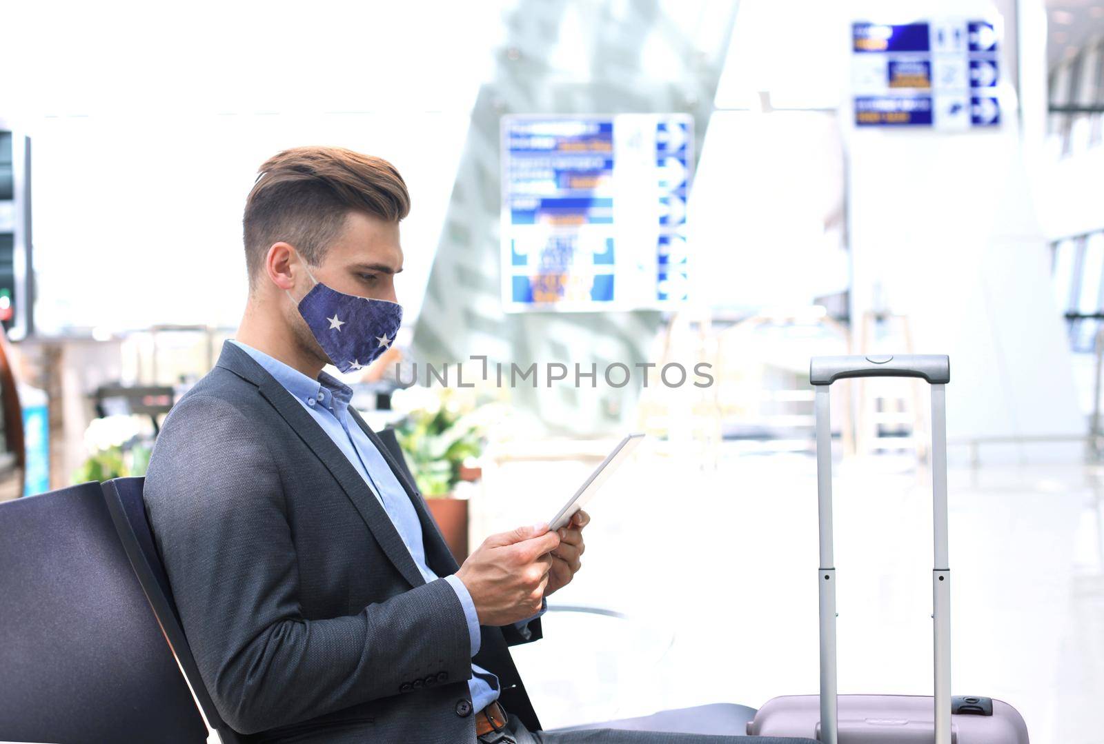 Businessman in protective mask with suitcase using digital tablet in hall of airport. Airport in the coronavirus epidemic. by tsyhun