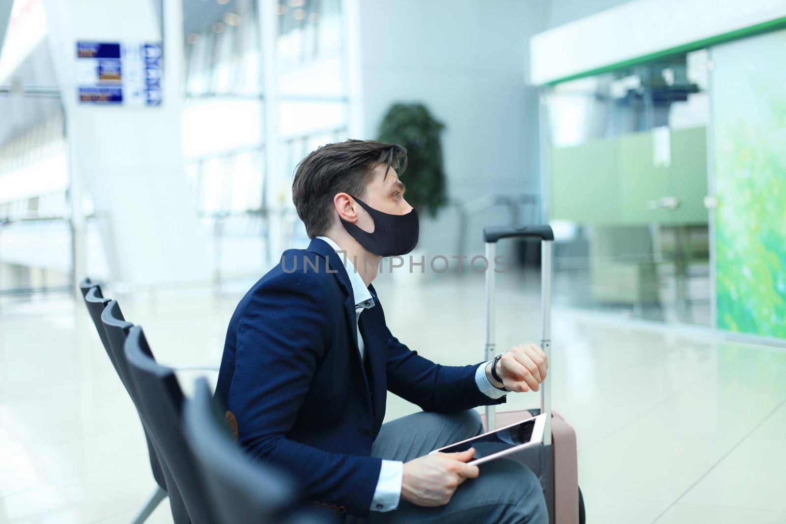 Businessman in protective mask with suitcase in hall of airport. Airport in the coronavirus epidemic. by tsyhun