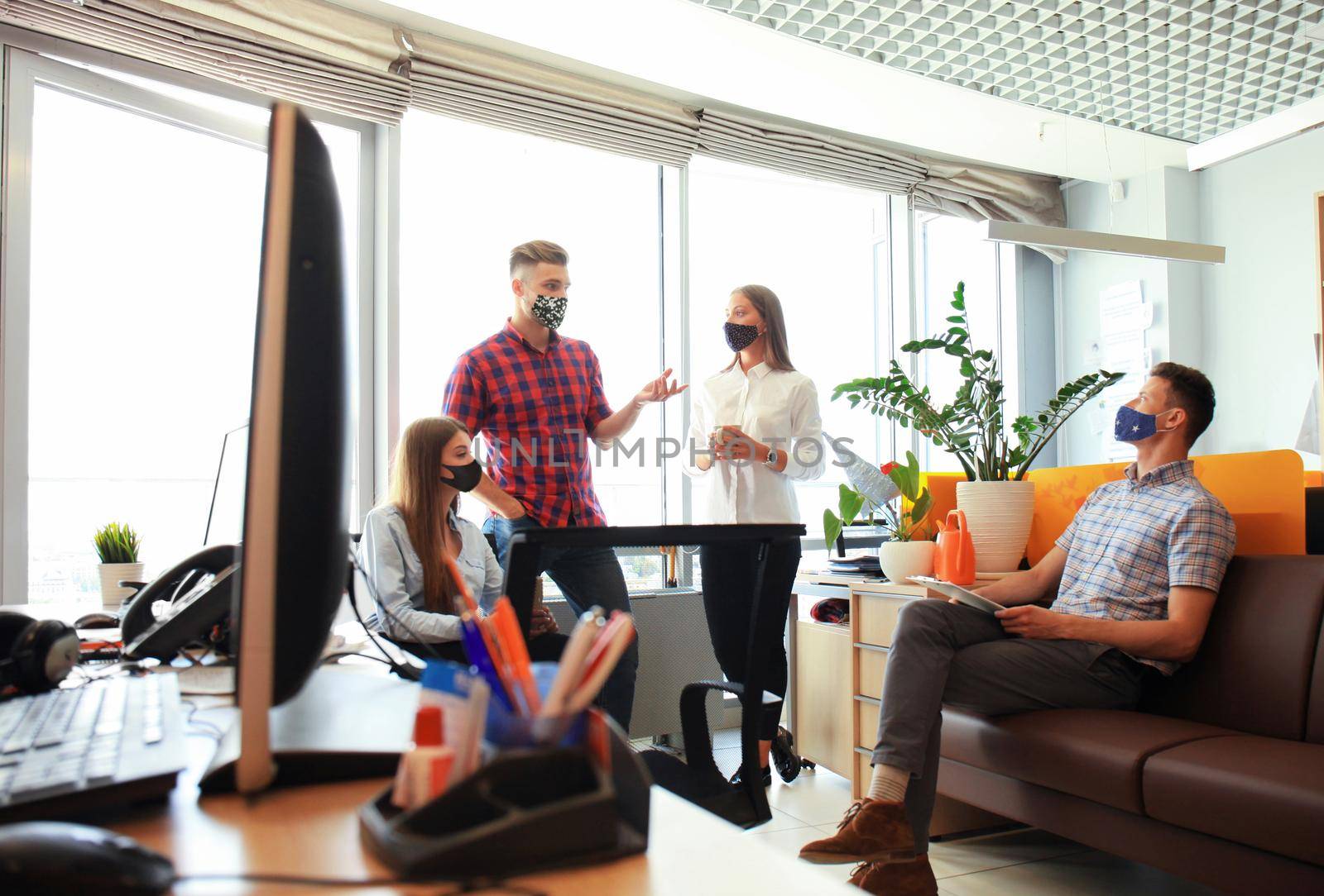 Startup business team in protective masks on meeting in modern bright office interior discussing new project