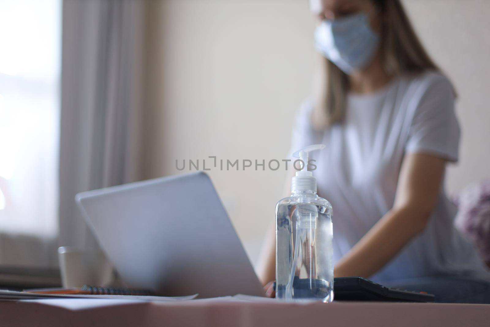Young woman works from home during self isolation and quarantine. Sanitizer hand gel is on the table. Work online and stay at home. by tsyhun
