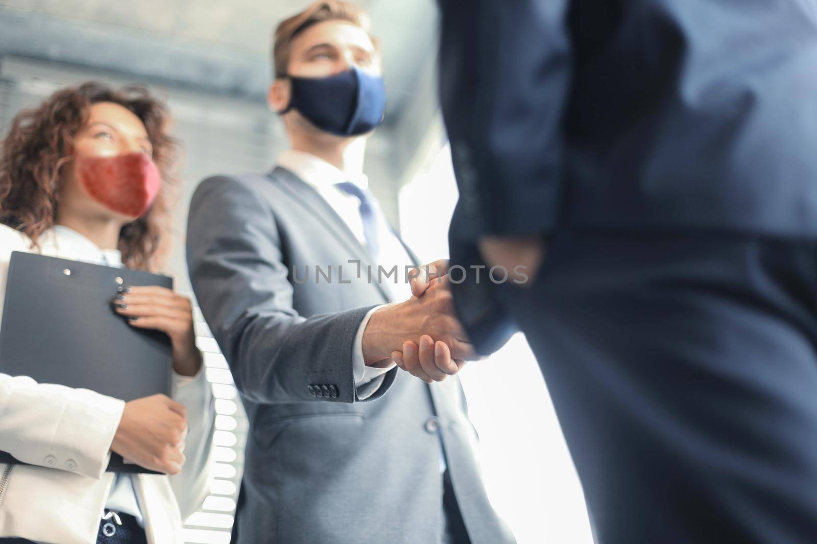 Business people in protective masks shaking hands, finishing up a meeting. by tsyhun