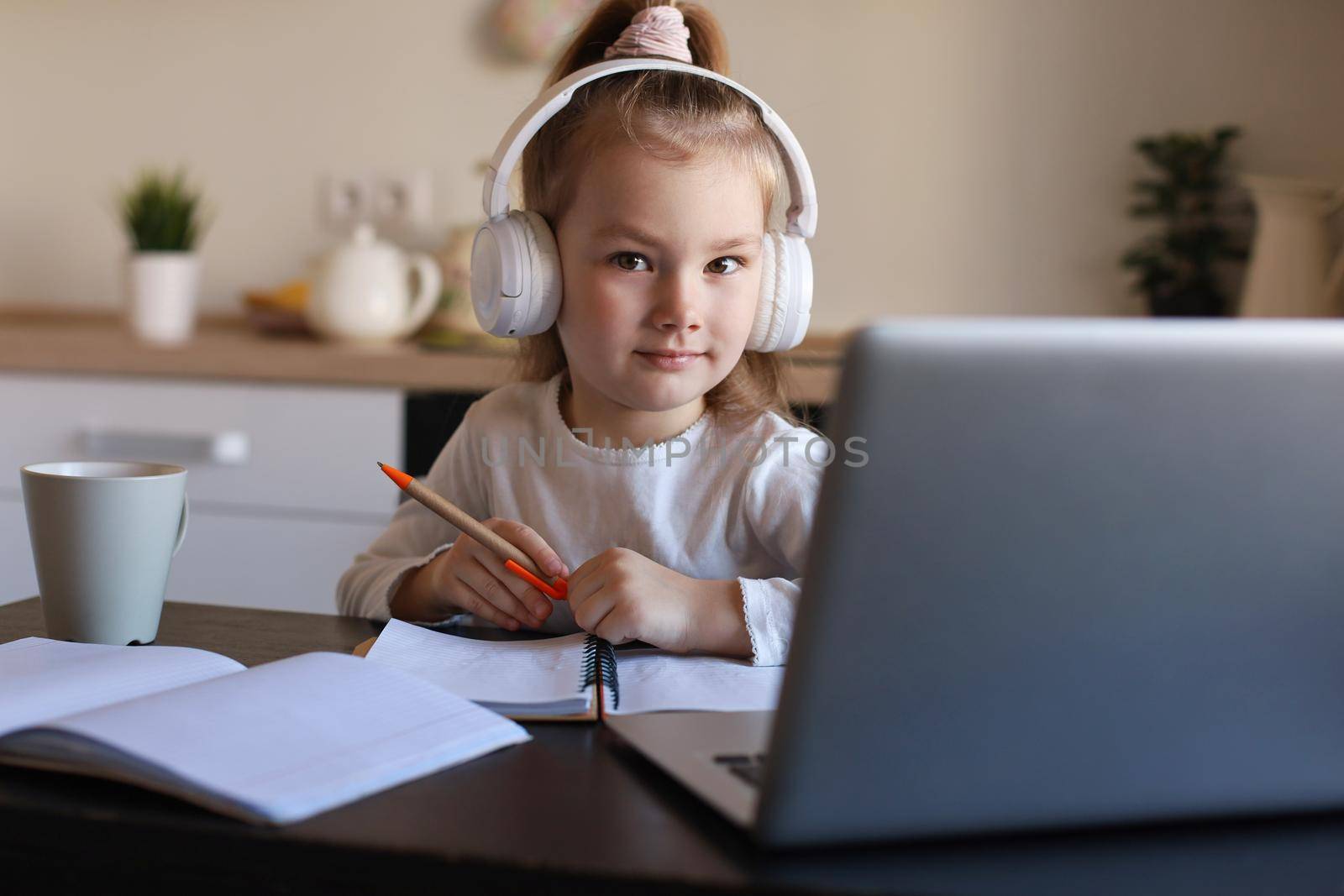 Smiling little girl in headphones handwrite study online using laptop at home, cute happy small child in earphones take Internet web lesson or class on PC. by tsyhun