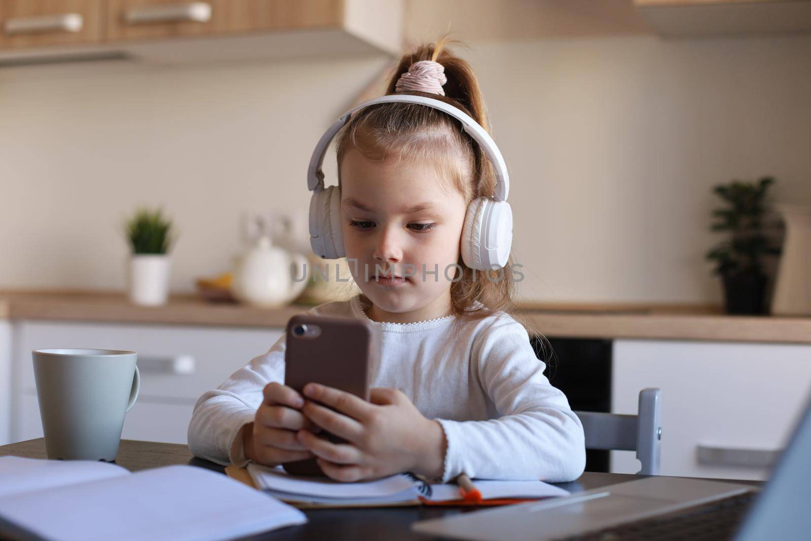 Smart little girl in headphones do homework online class on smartphone, small child in earphones study on Internet, have web conference or lesson during quarantine. by tsyhun