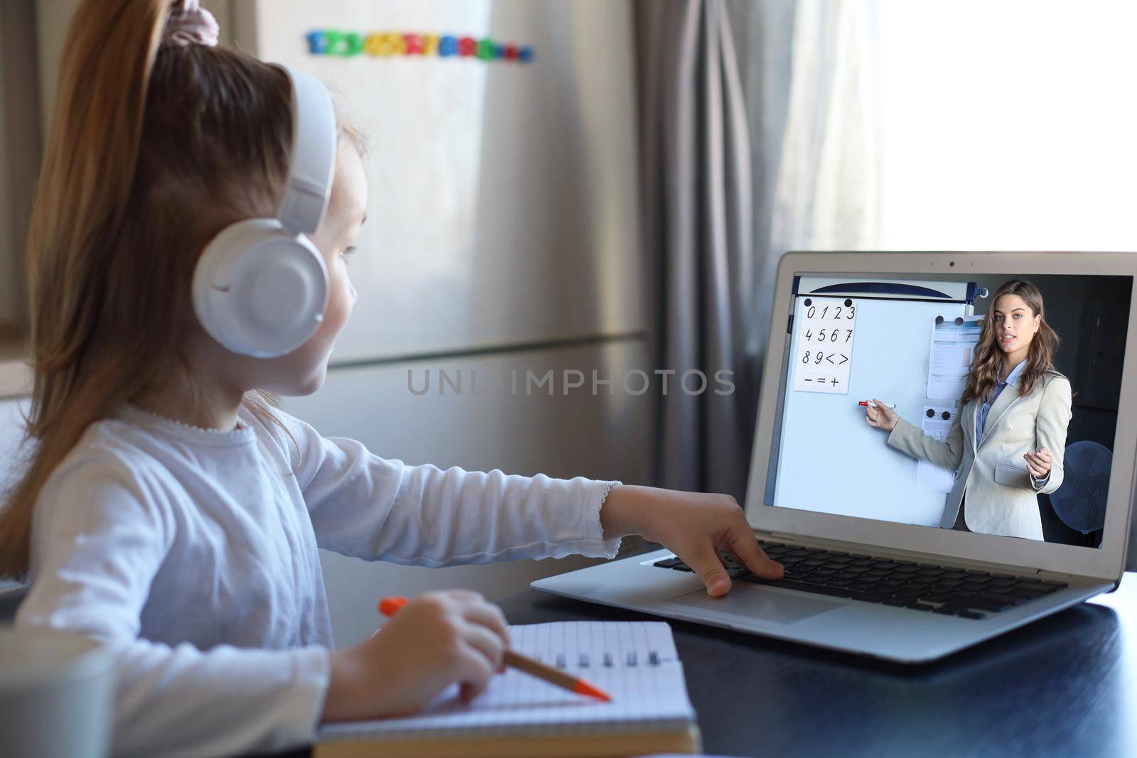 Smart small preschooler girl in headphones watch online lesson and communicate with teacher at home, little child in earphones study on Internet using laptop wireless connection. by tsyhun