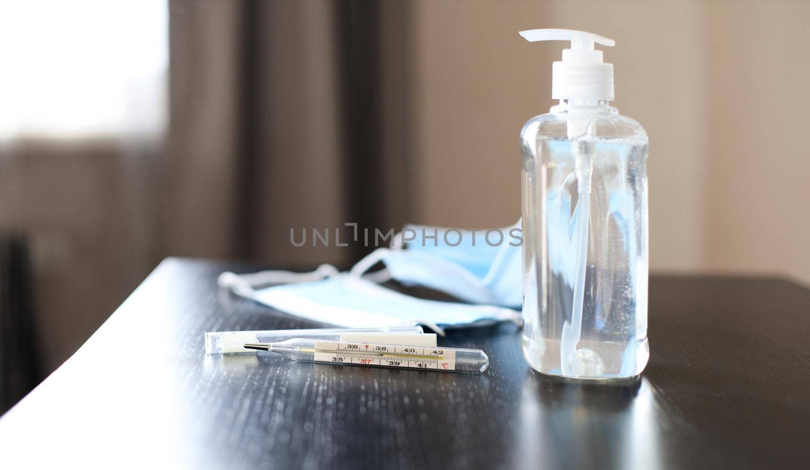 Analogue medical thermometer showing high temperature, prevention medical surgical mask and sanitizer gel for hand hygiene corona virus protection lies on table.