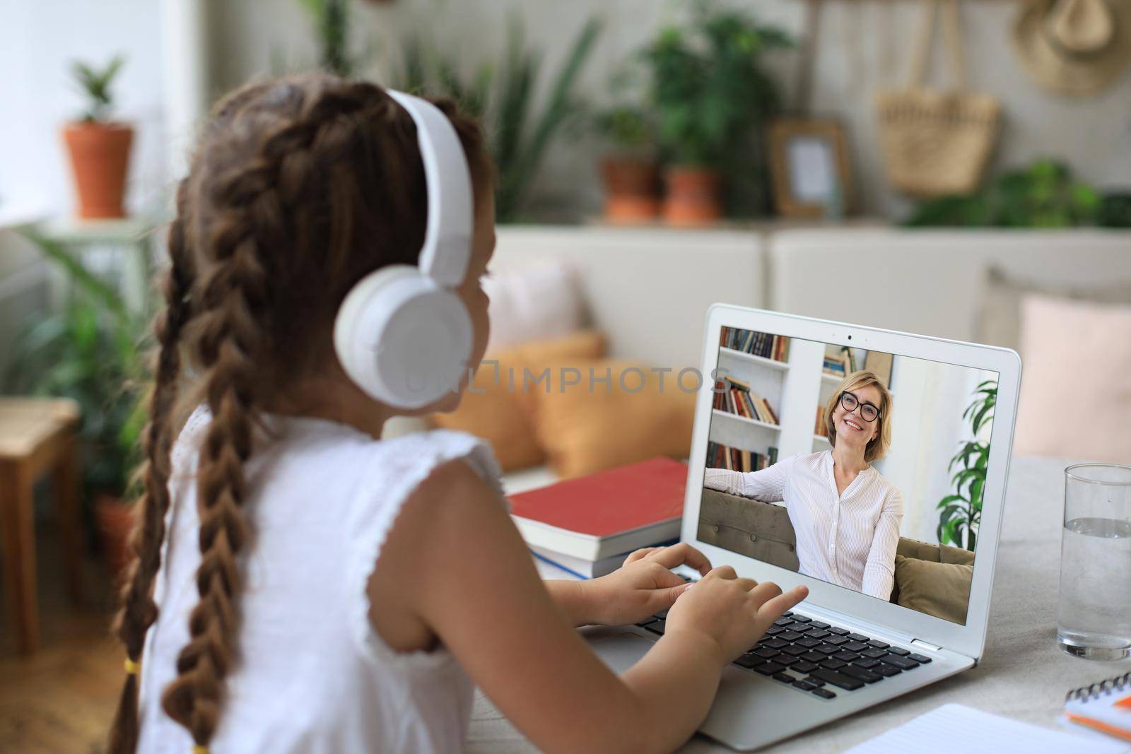 Distance learning. Cheerful little girl girl in headphones using laptop studying through online e-learning system