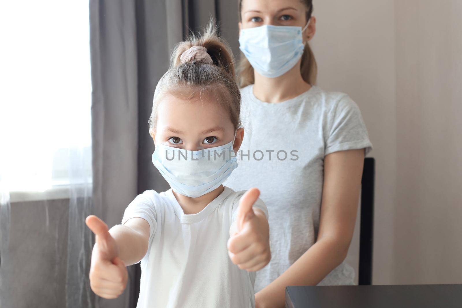 Little girl with her mother in a medical masks showing thumb's up gesture. Protection against coronavirus