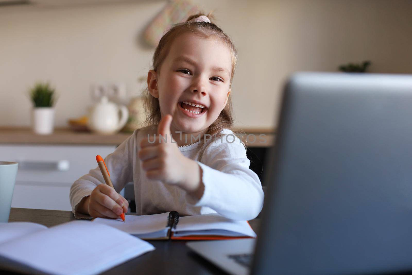 Happy little girl pupil study online using laptop at home, smiling small child show thumb up recommend class or lesson. by tsyhun
