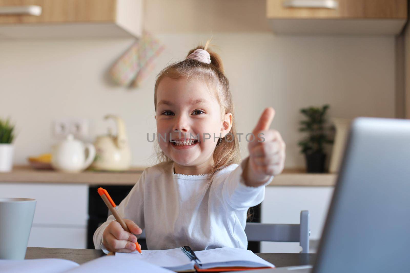 Happy little girl pupil study online using laptop at home, smiling small child show thumb up recommend class or lesson