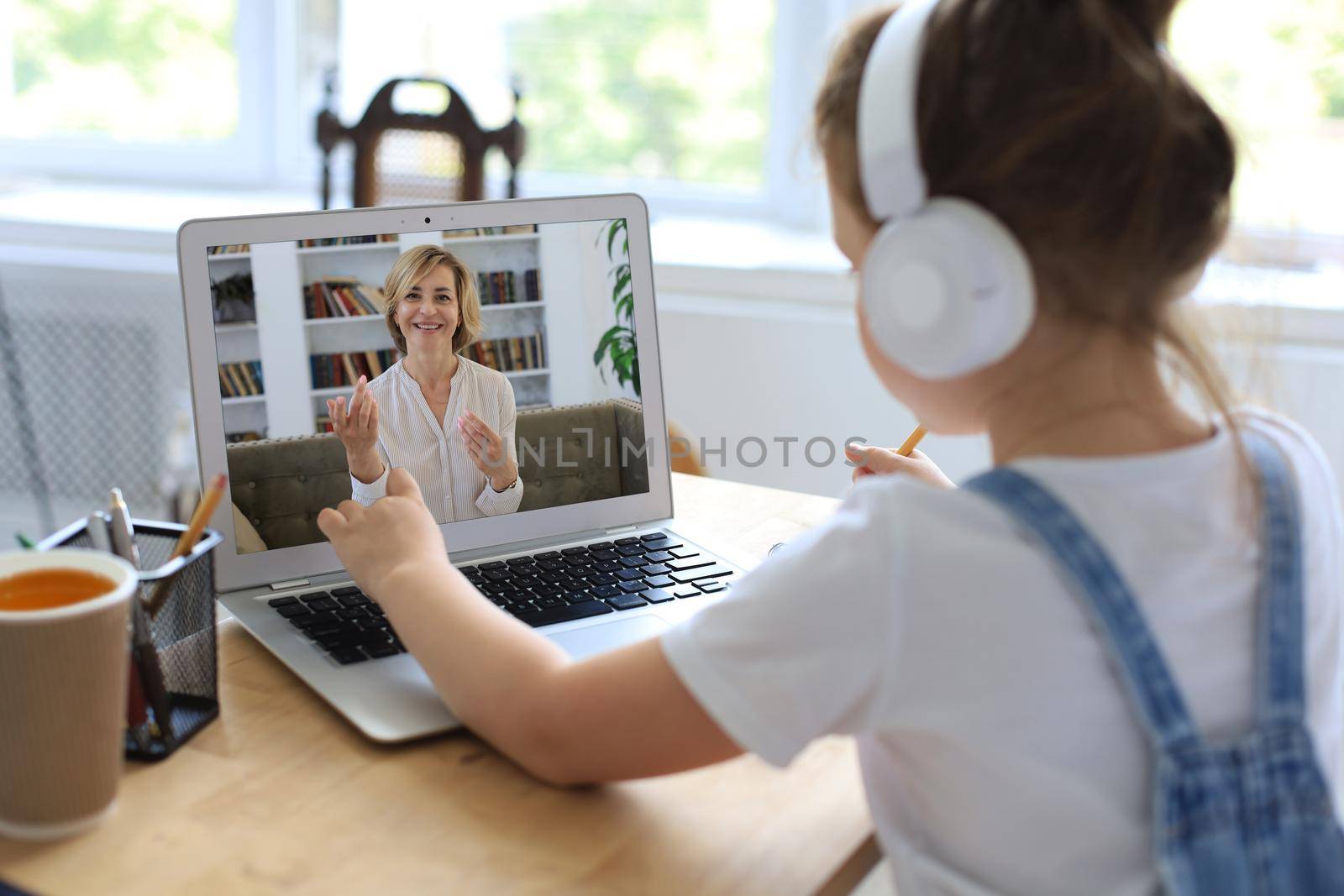 Distance learning. Cheerful little girl girl in headphones using laptop studying through online e-learning system. by tsyhun