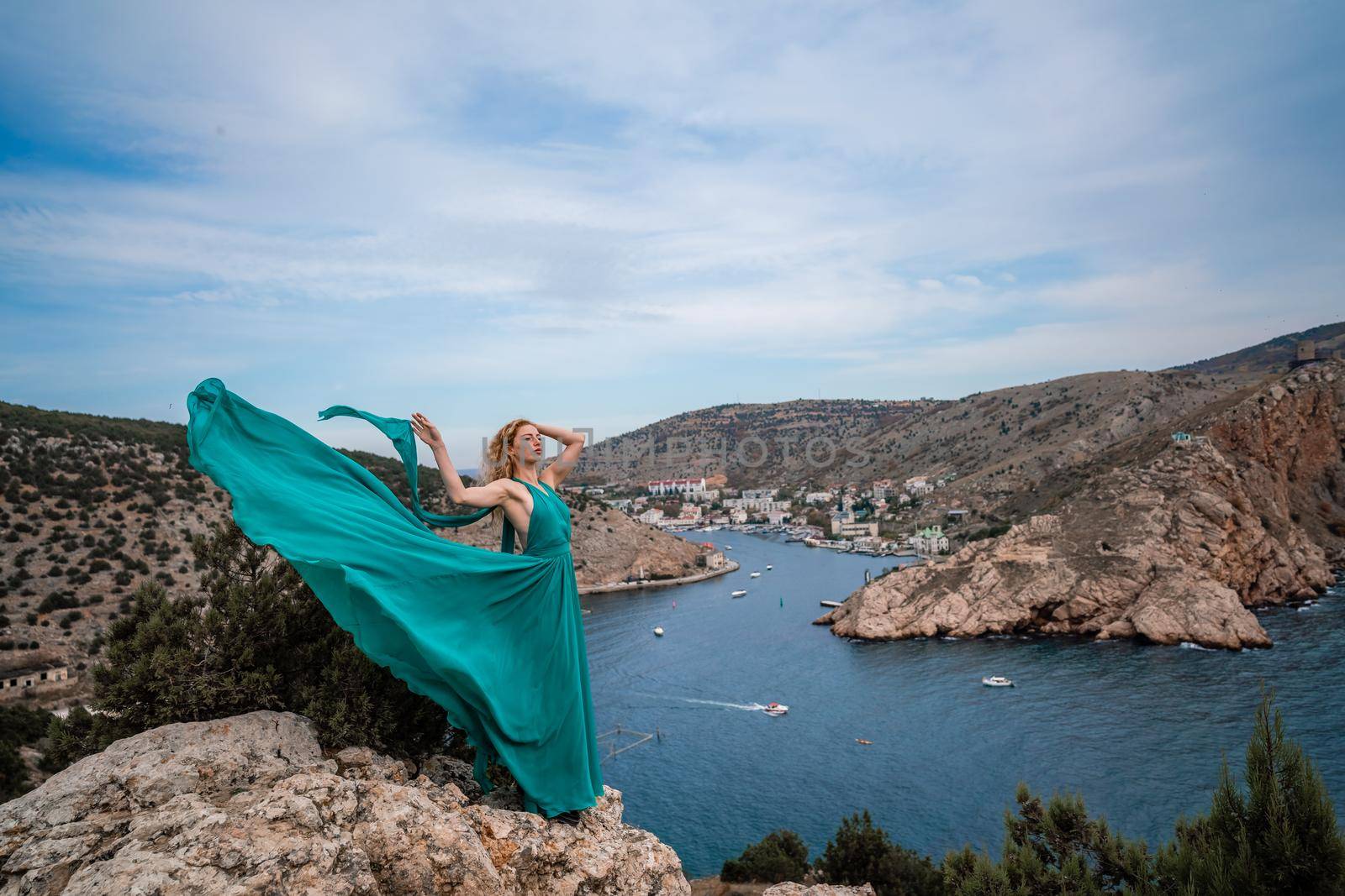 A woman in an emerald dress, a fashion model with long silk wings in a flowing dress, flying fabric on the embankment