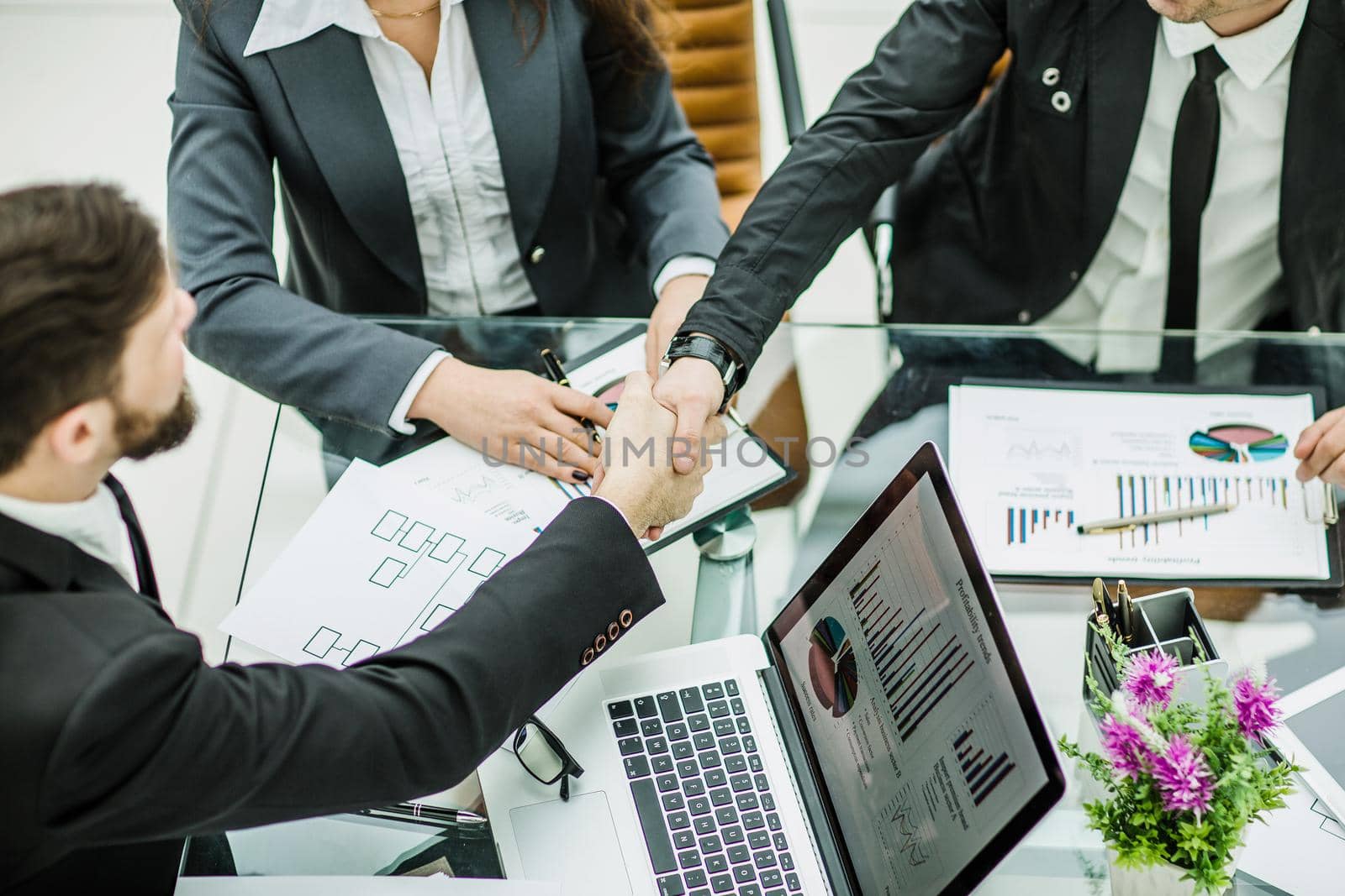 handshake of business partners on the background of financial graphs lying in the workplace