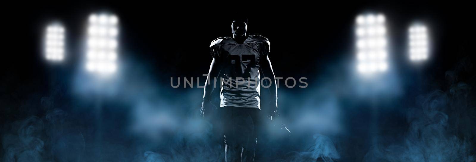 portrait of young confident American football player on field at night