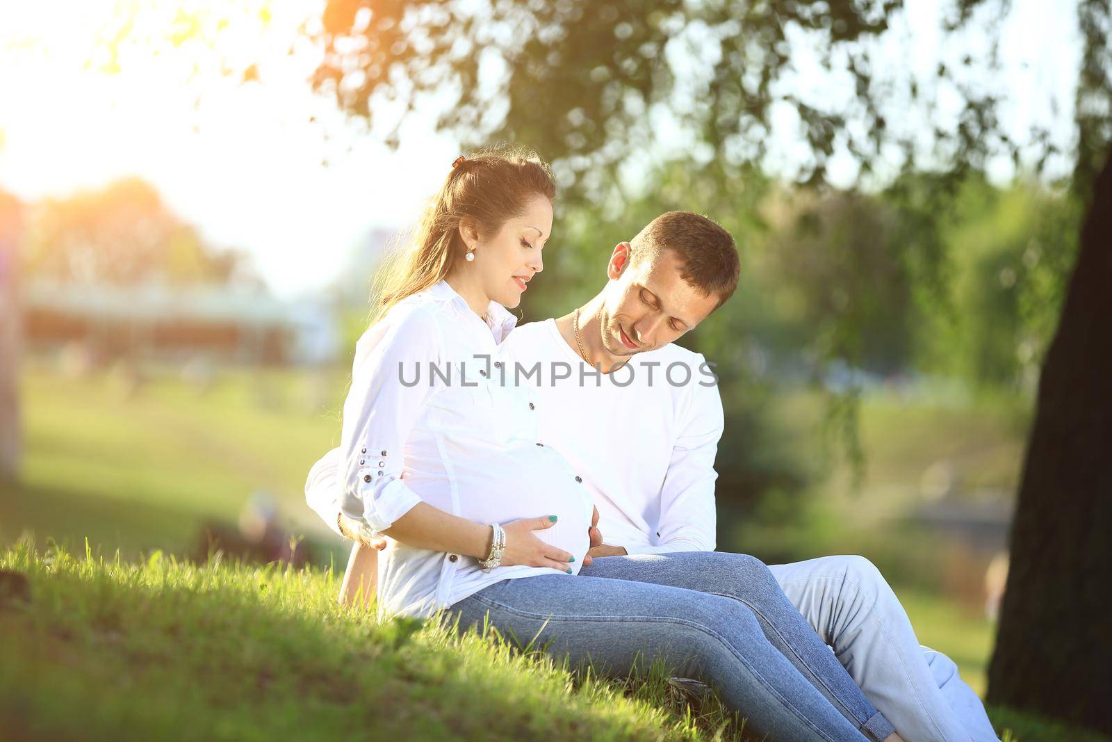 pregnant woman and happy future father sitting on the grass in the Park on a Sunny day