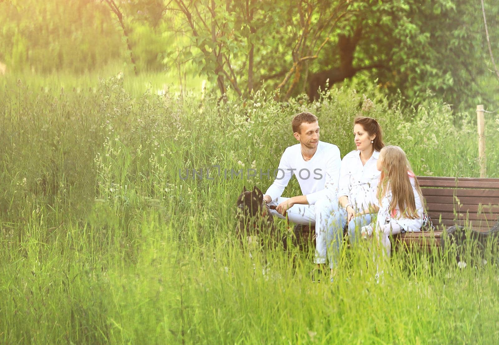 little girl with parents sits on a Park bench in summer Sunny day.the photo has a space for your text.