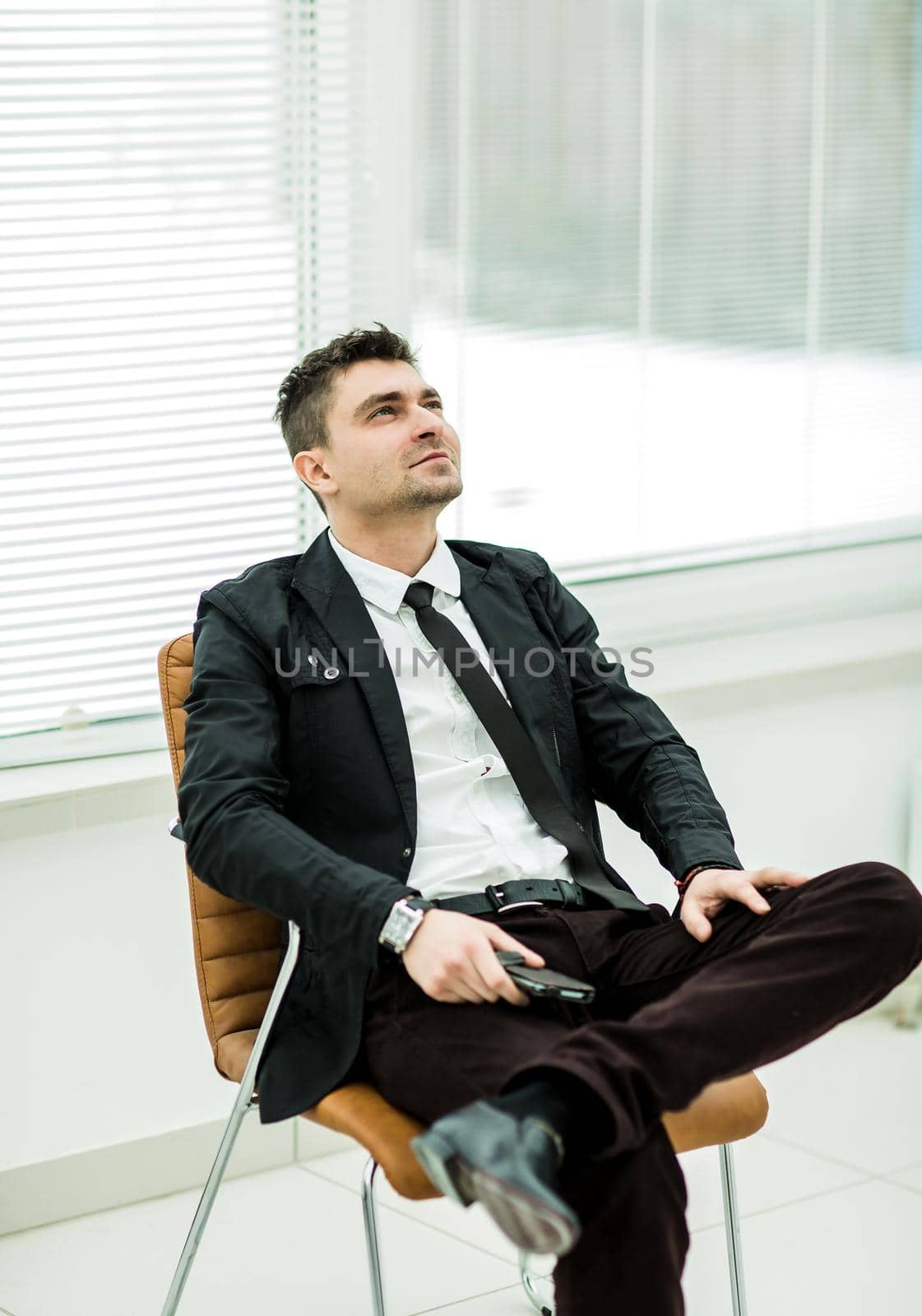 successful businessman with smartphone sitting in a chair in a modern office .the photo has a empty space for your text