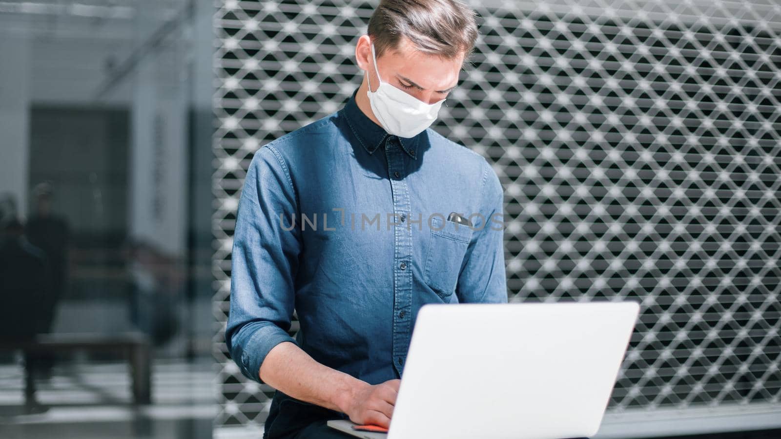 man in a protective mask spraying a bactericidal spray on the surface of a laptop. by SmartPhotoLab