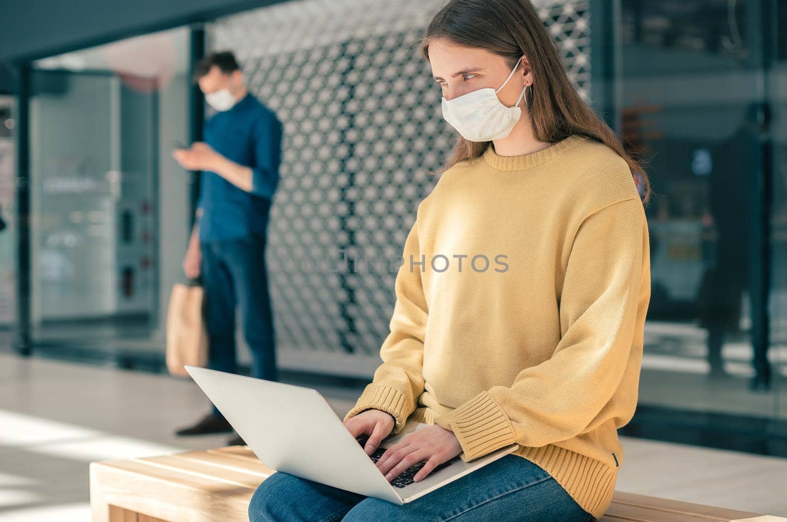 female blogger in a protective mask works on a laptop by SmartPhotoLab