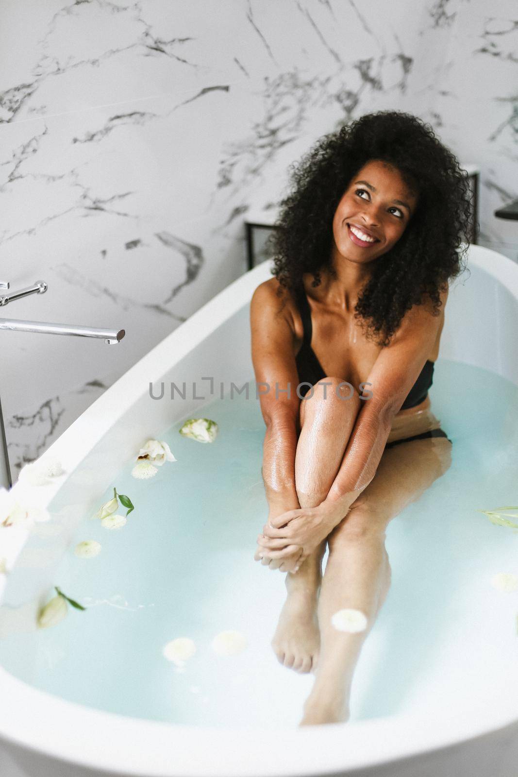 Young relaxed afro american girl sitting in bath, wearing black swimsuit. by sisterspro