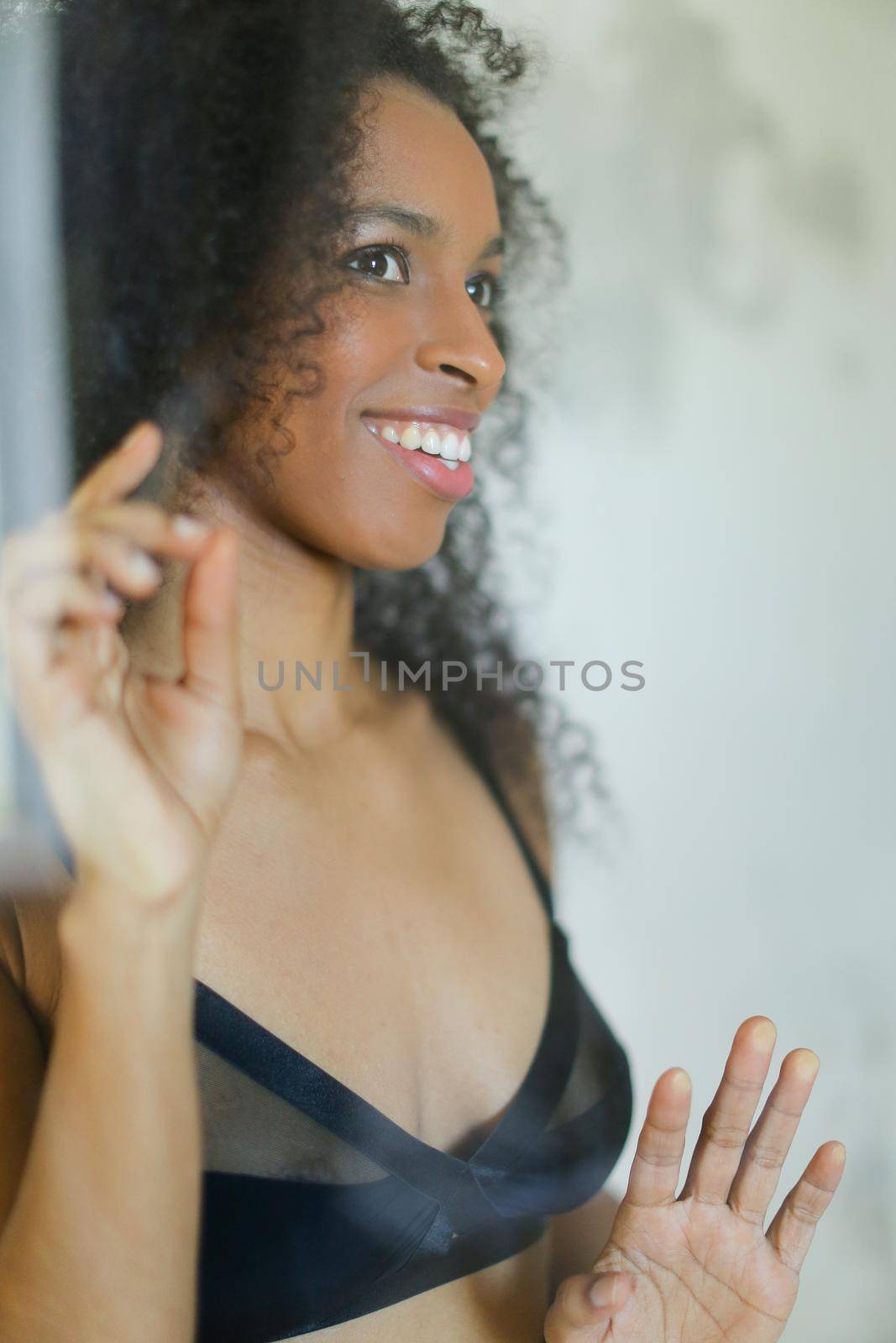 Portrait of young afro american smiling nice young woman wearing bra and touching glass in bathroom. Concept of underwear photo session.