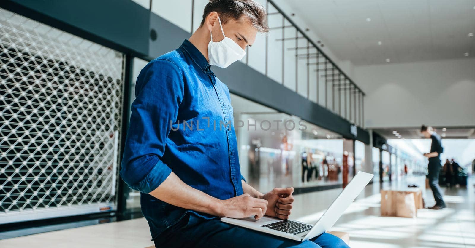 man in a protective mask works on a laptop in a shopping center building. by SmartPhotoLab