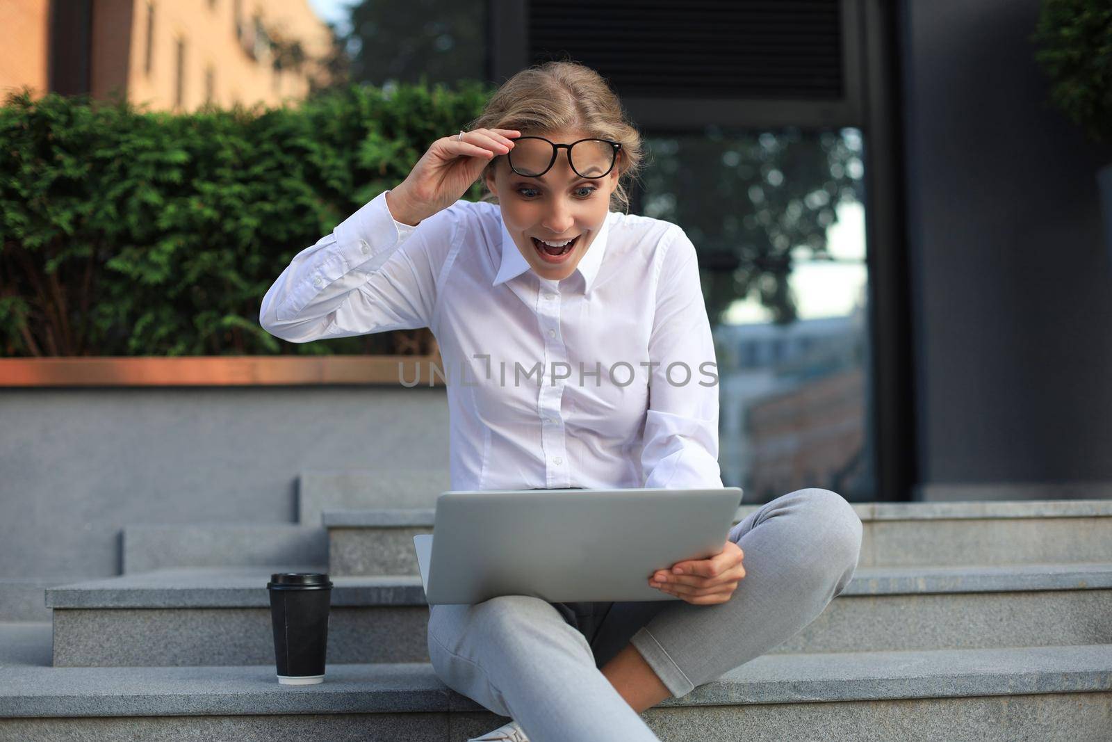 Beautiful excited business woman sitting near business center and using laptop