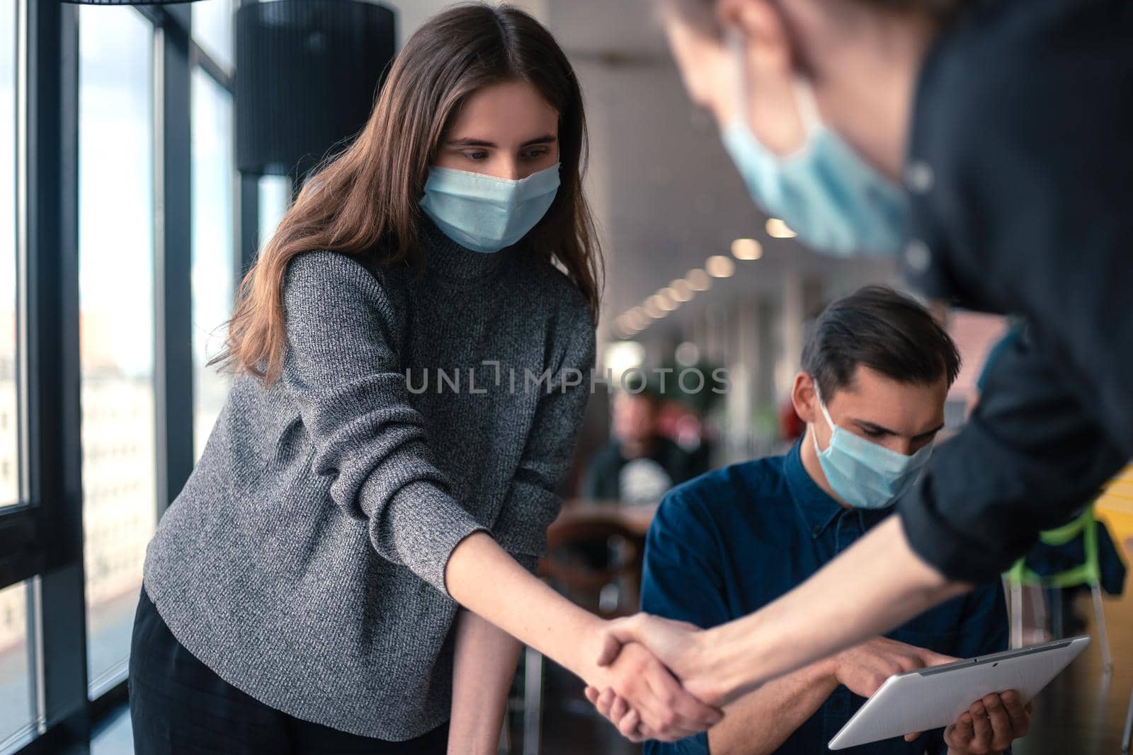 young staff in protective masks shaking hands with each other. by SmartPhotoLab