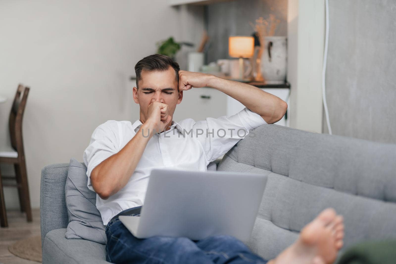 yawning young man with a laptop is resting in the living room. by SmartPhotoLab