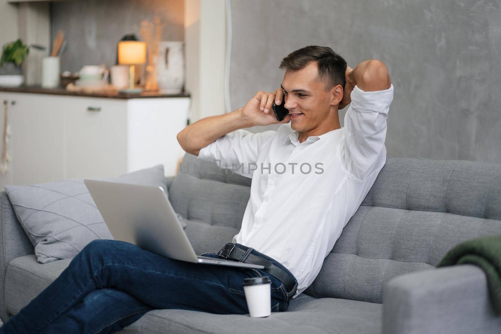 young man with a laptop talking on a smartphone. by SmartPhotoLab