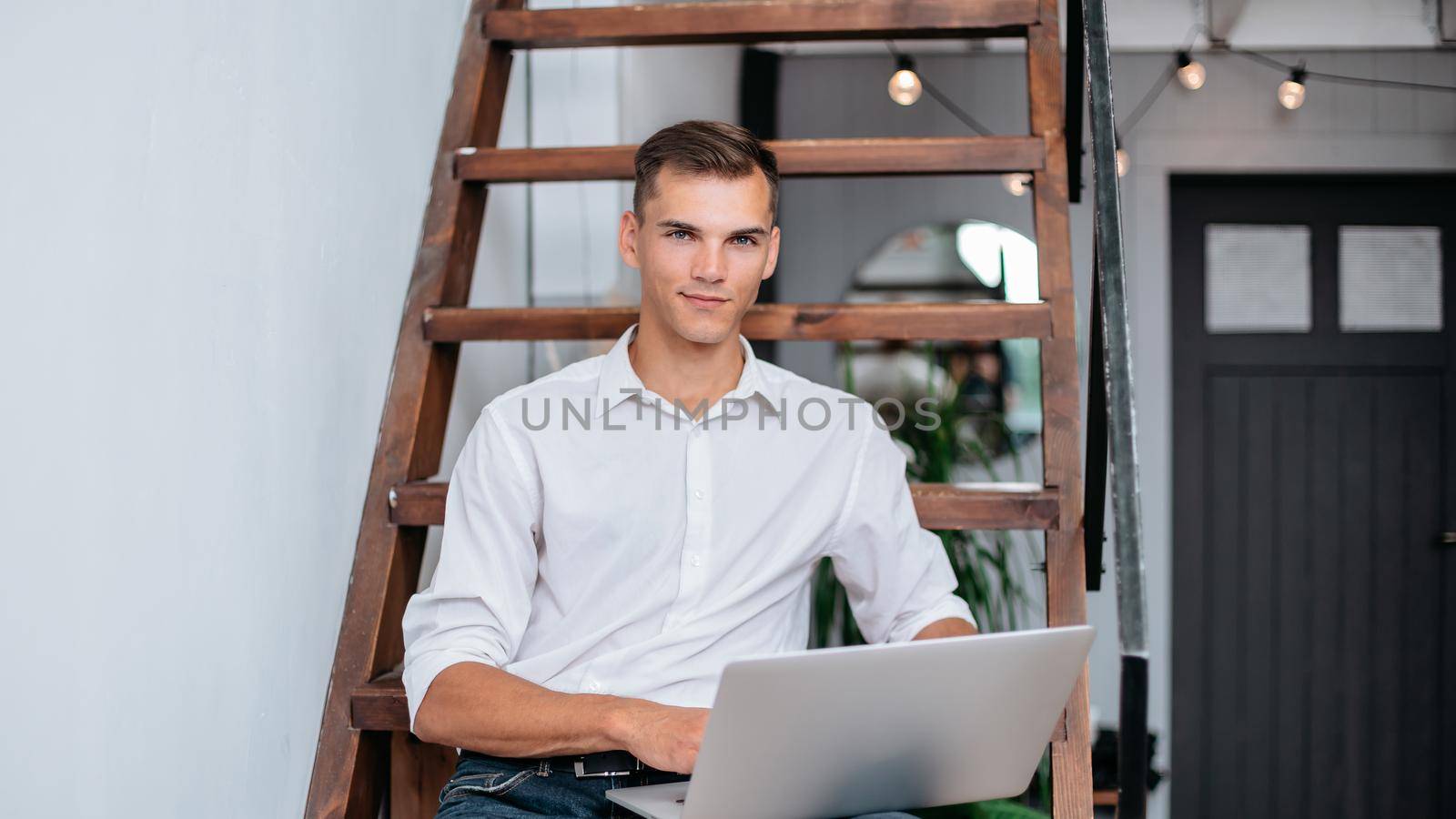 young man with a laptop sitting on the steps in his apartment. by SmartPhotoLab