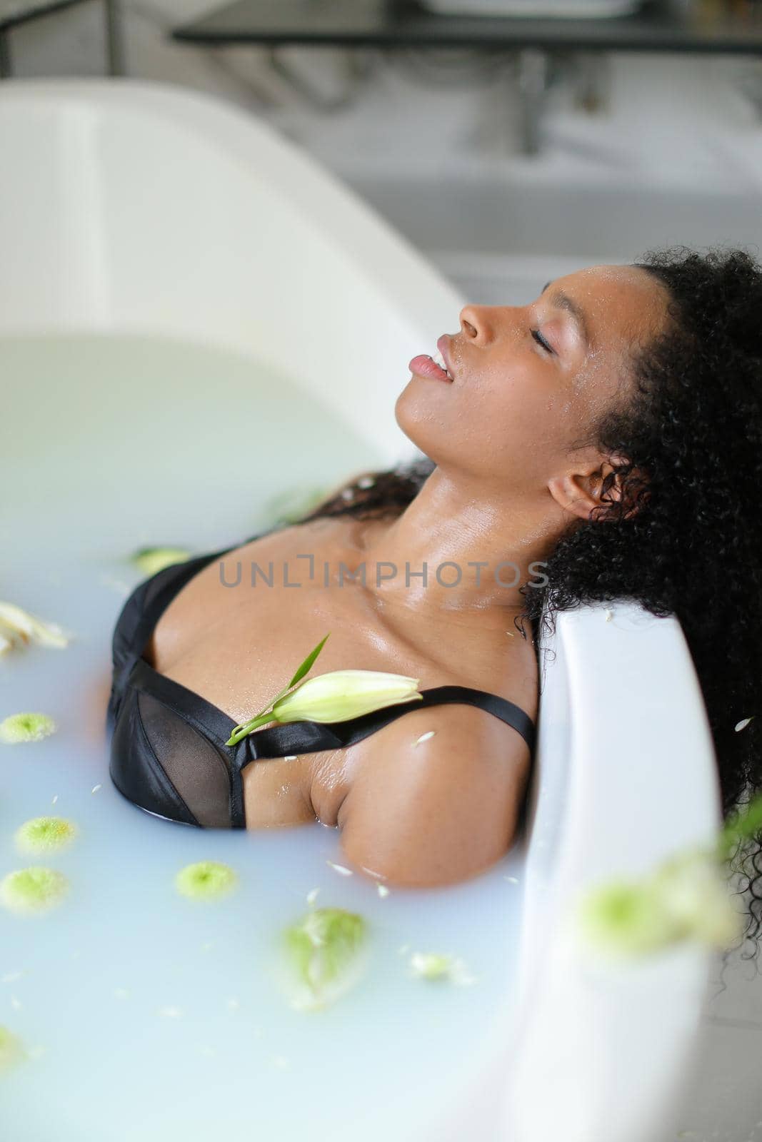 Black relaxed young girl lying in milk bath and wearing swimsuit. by sisterspro