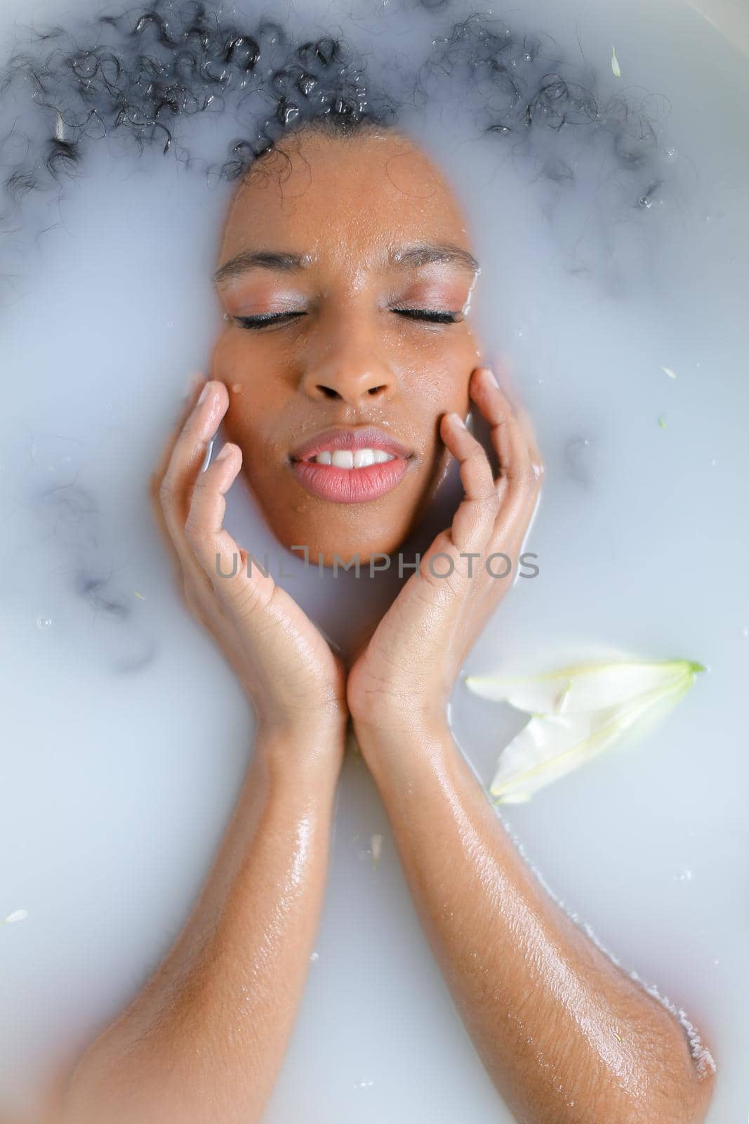 Close up portrait of beautiful afro american woman with closed eyes taking milk bath. Concept of spa and aromatherapy.