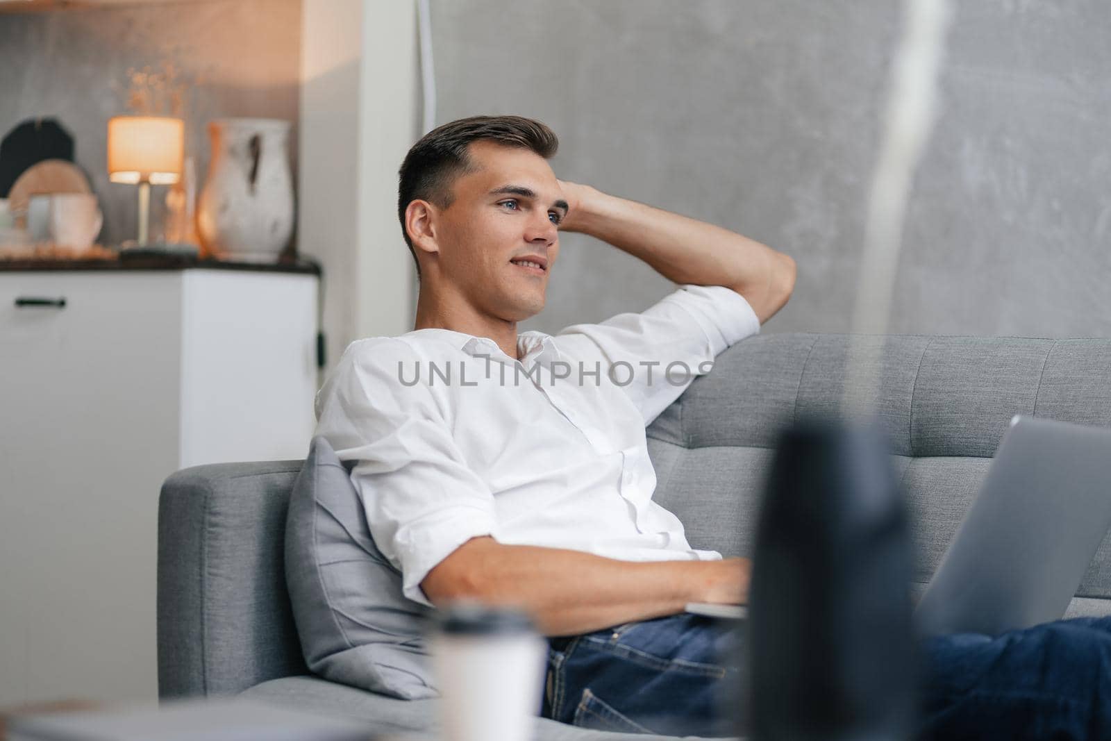 thoughtful young man with a laptop sitting on the couch. by SmartPhotoLab