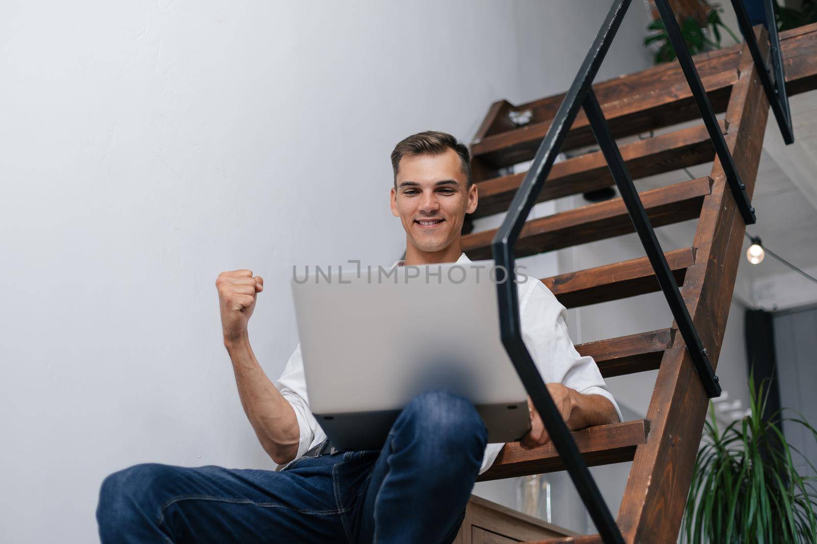 happy man with a laptop sitting on the steps in his apartment. photo with a copy-space.