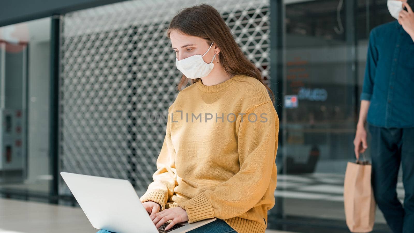 young woman is working on a laptop while sitting outside a city building. pandemic in the city