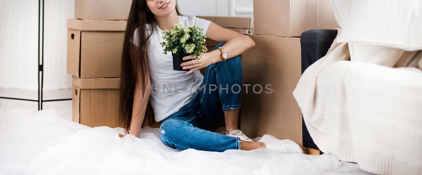 young woman with a home plant sitting on the floor in the new living room. photo with copy-space