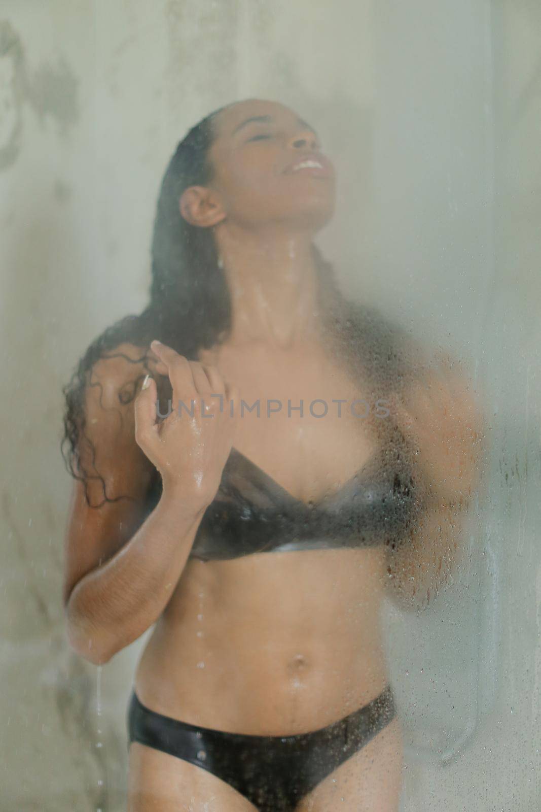 Slim black girl taking shower and wearing swimsuit, water drops on glass. by sisterspro