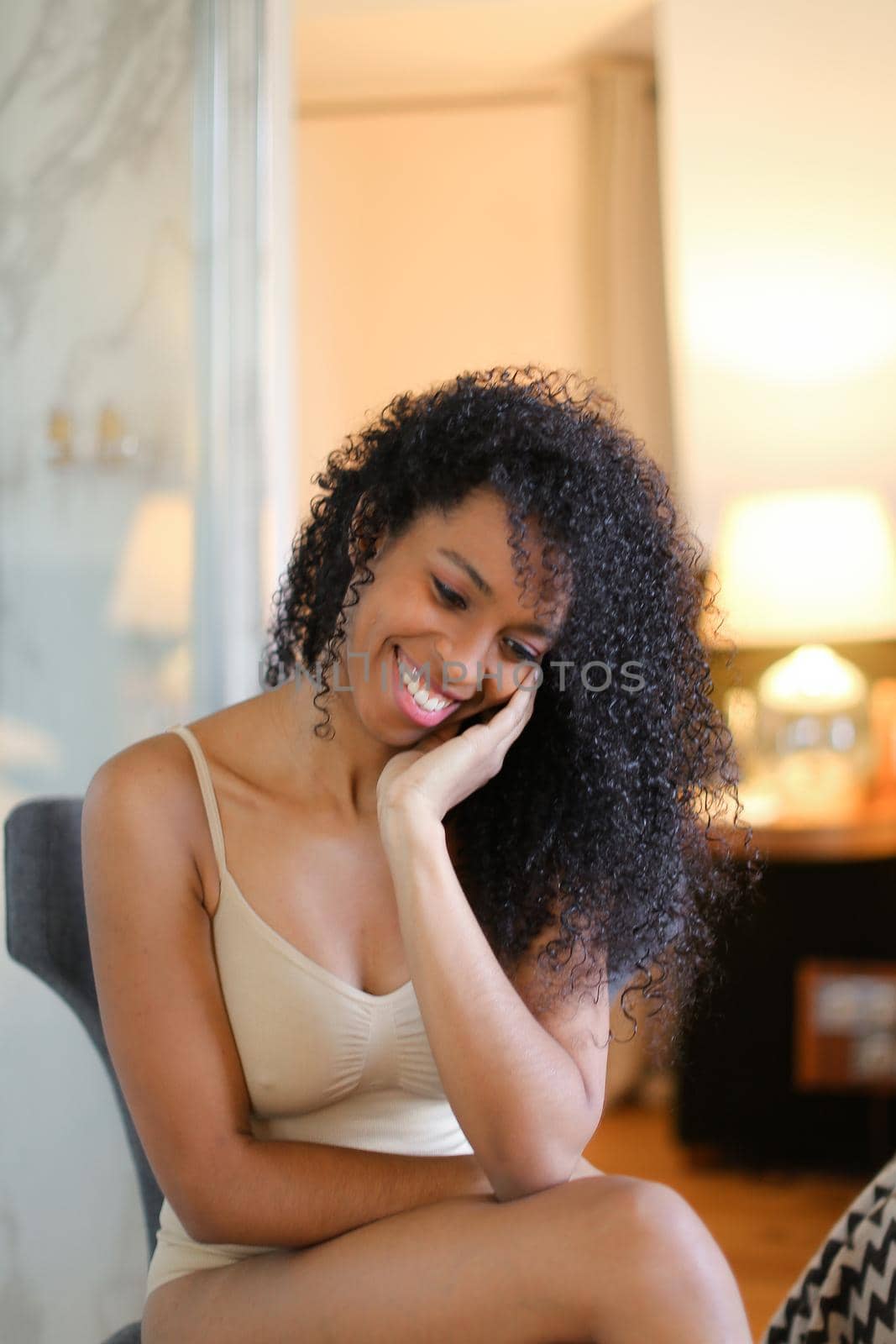 Young pretty afro american woman sitting in room and wearing beige swimsuit. Concept of hotel photo session in lingerie.