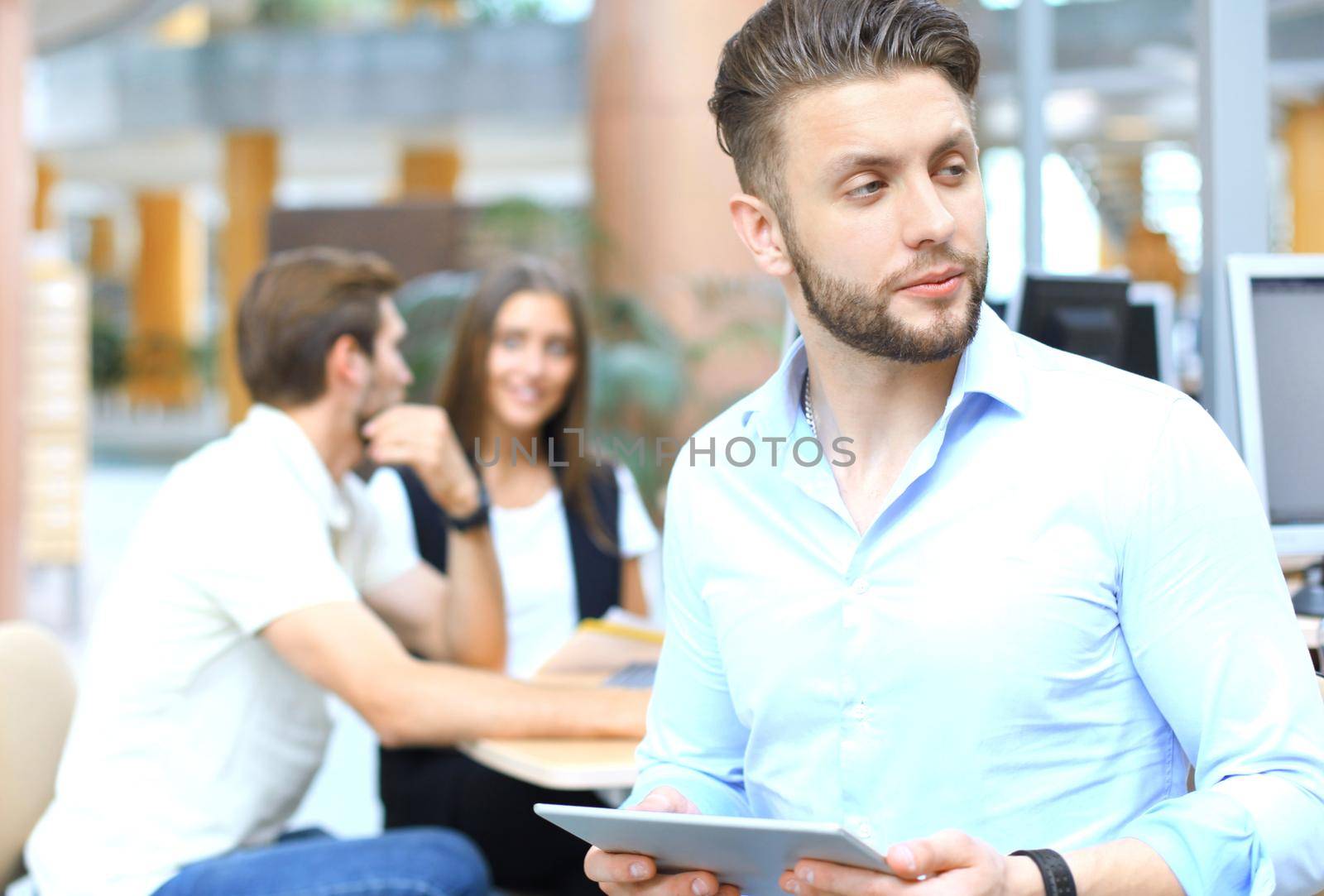 Young man holding digital tablet while his colleagues working in the background.