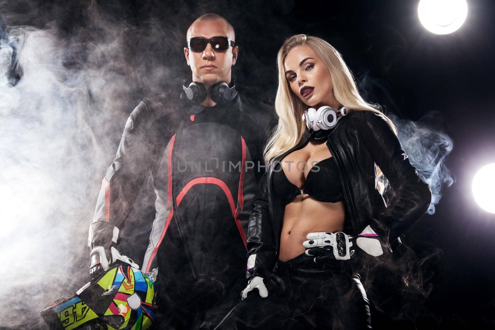 Fashion couple model DJ and biker with headphones and sunglasses, black leather jacket, leather pants, stylish pretty blonde woman and man in night casual outfit. Long wavy hairstyle. by MikeOrlov