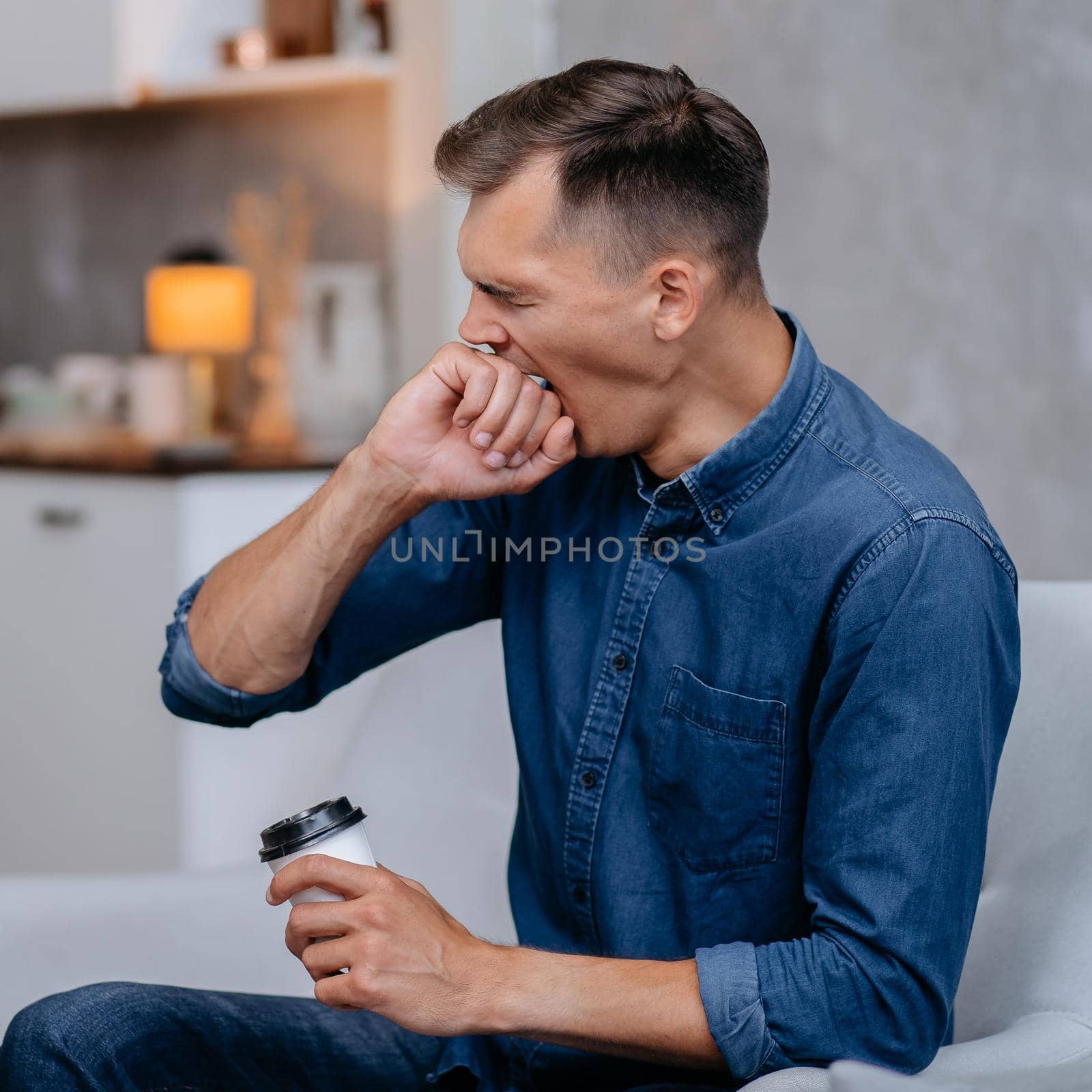 yawning young man with a Cup of coffee sitting in a chair . home life.