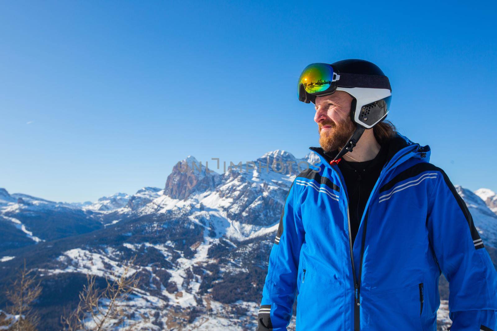 Happy smiling man skier in blue clothes on slope with mountains in the background at Cortina d'Ampezzo Faloria skiing resort area Dolomiti Italy