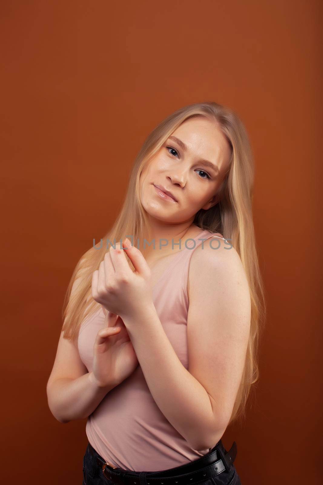 young pretty girl with blond hair posing cheerful on brown background, lifestyle people concept close up