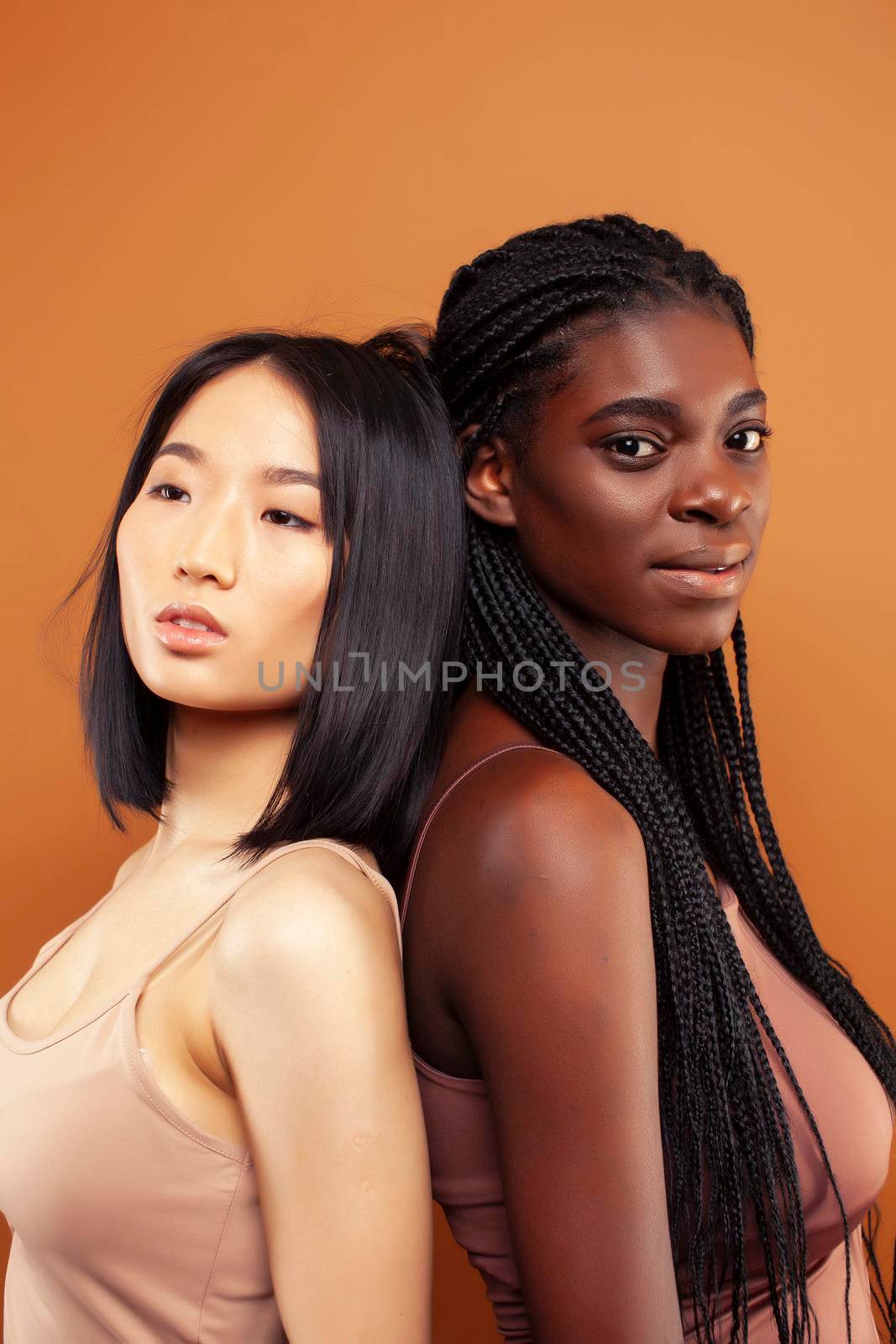 young pretty asian, african woman posing cheerful together on brown background, lifestyle diverse nationality people concept close up