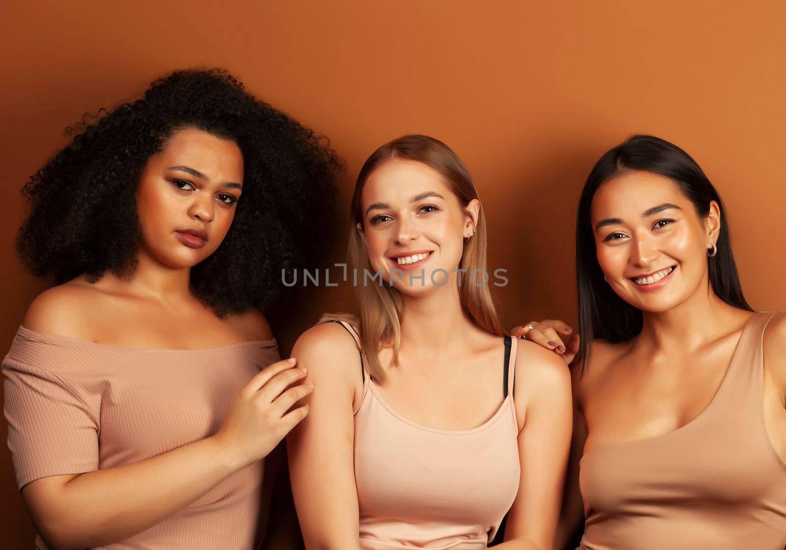 young pretty asian, caucasian, afro woman posing cheerful together on brown background, lifestyle diverse nationality people concept close up